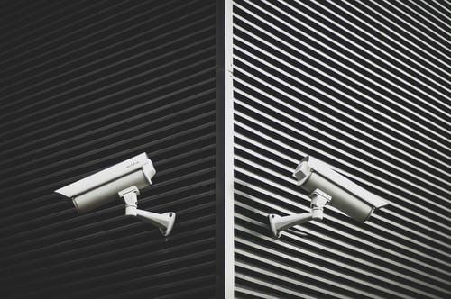 two-white-cctv-cameras-on-grey-slat-walls-across-corner