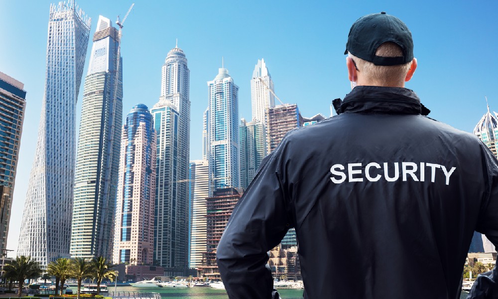 security guard in black jacket facing a marina beside a city