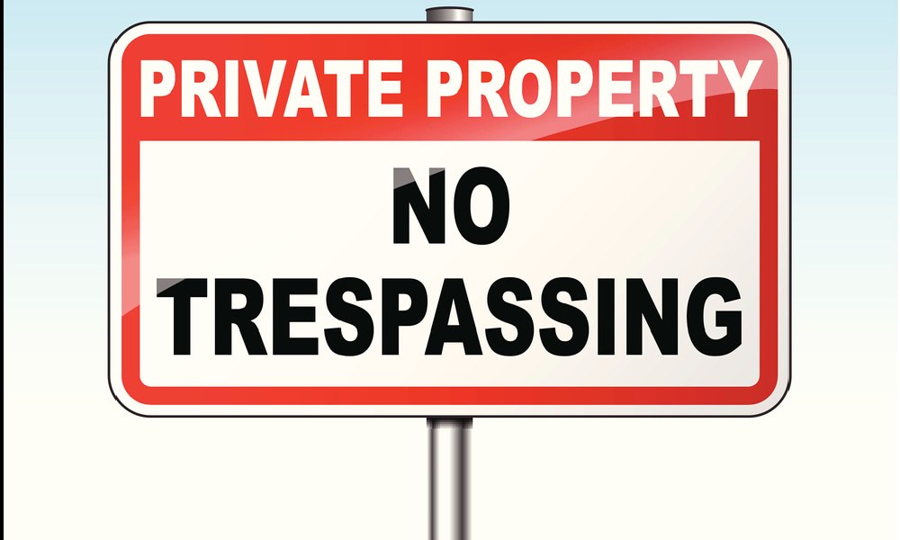 A red and white warning sign reads “PRIVATE PROPERTY NO TRESPASSING,” illustrating the signage required in many states’ trespassing laws.